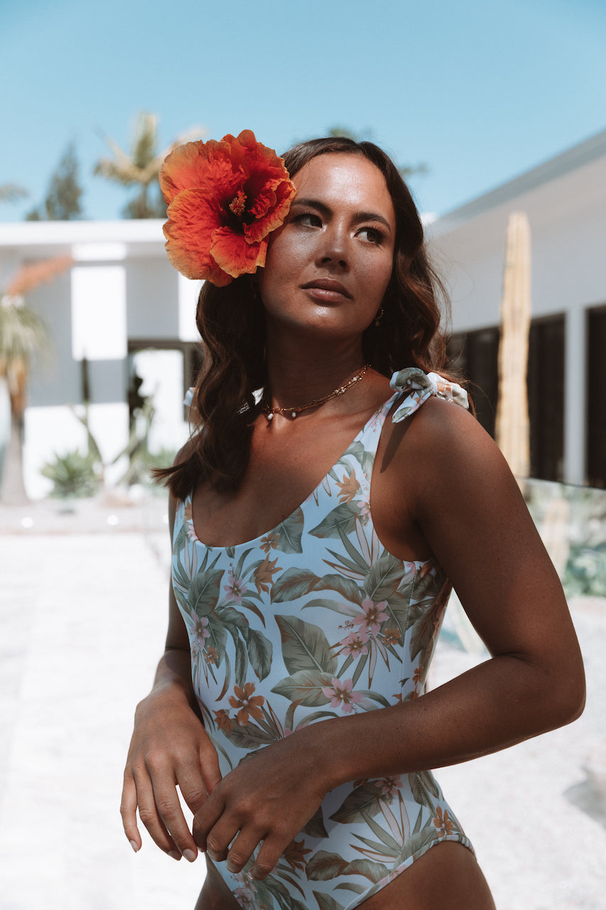 Palm Springs One piece. Featuring our new Palm Springs Print! This super cute one piece has a flattering fit and adjustable tie shoulder straps. Made from recycled materials, this soft fabric is double lined and seamless. With a very low 'v' shaped back and a medium coverage bottom. This piece is the perfect Summer staple! It has been designed for use in the water and out, and looks great paired with denim shorts or skirt and of course our matching scrunchie!